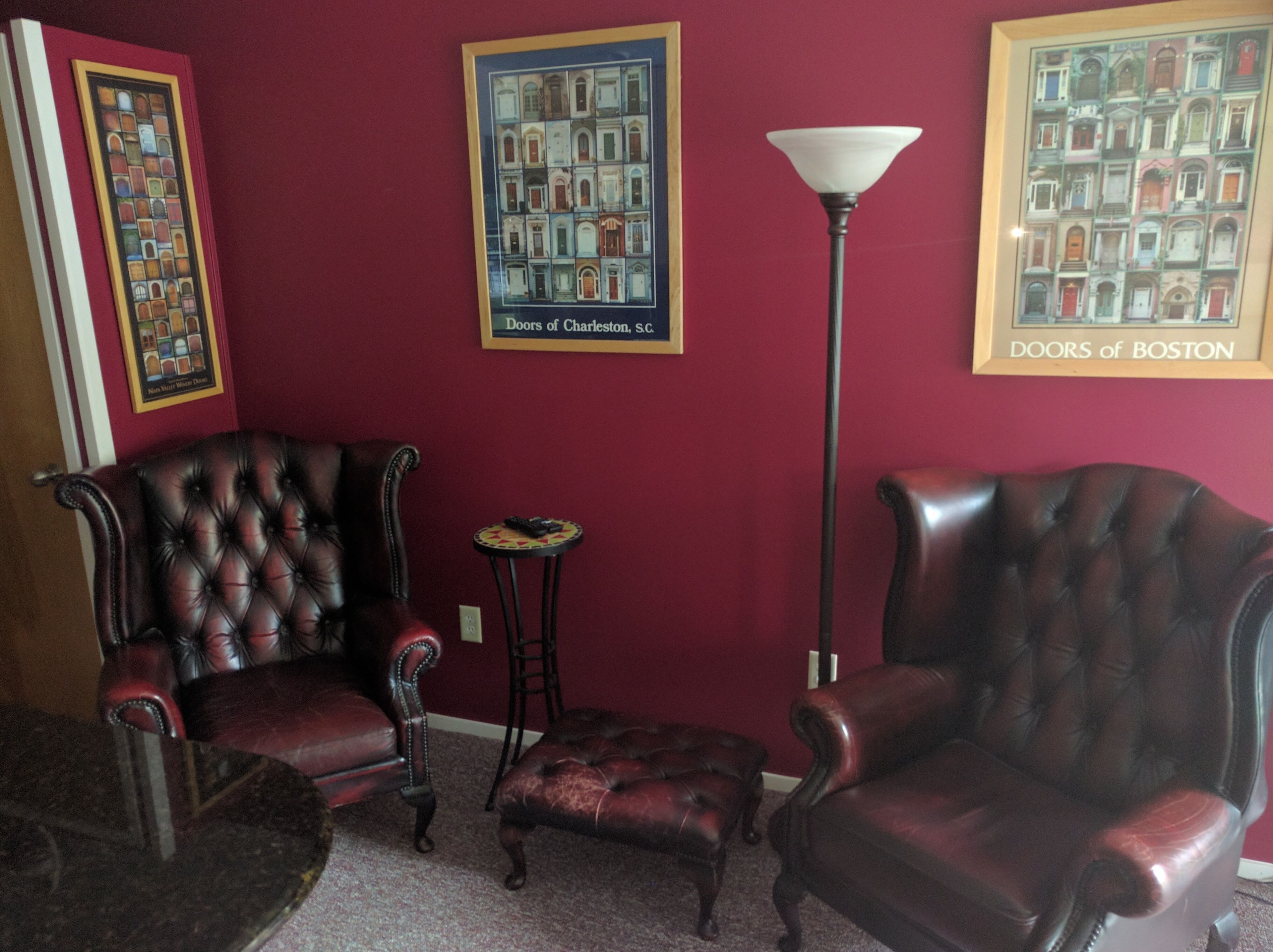Een kamer met twee leren fauteuils, een bijzettafeltje, een vloerlamp en twee ingelijste foto's van deuren.