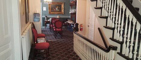 A hallway with a staircase, a dining area with red chairs, and a chandelier.