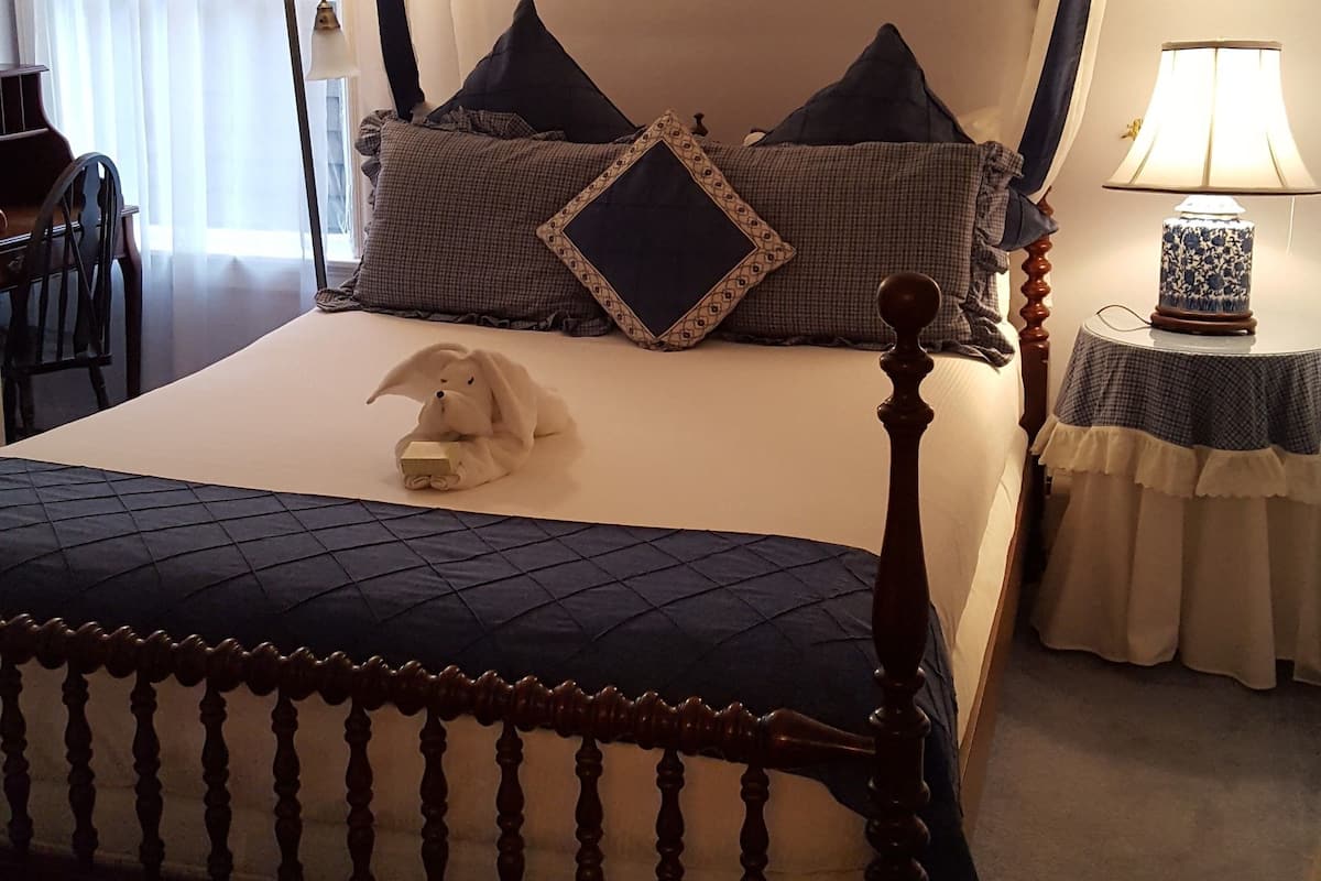 A four-poster bed with a canopy, a bedside table with a lamp, and a chair in a hotel room.