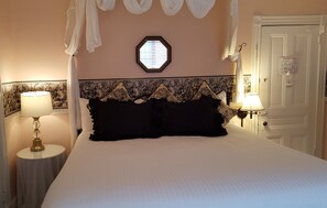 A neatly made bed with a white and black headboard, two bedside lamps, a wall-mounted mirror, and a door with a posted notice. - Cleveland House (Newport)