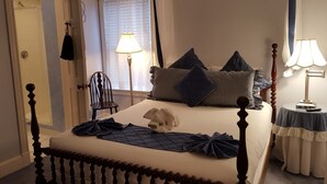 A neatly made bed with pillows and a blanket, a bedside table with a lamp, and a chair in a room with a door and window. - Cleveland House (Newport)