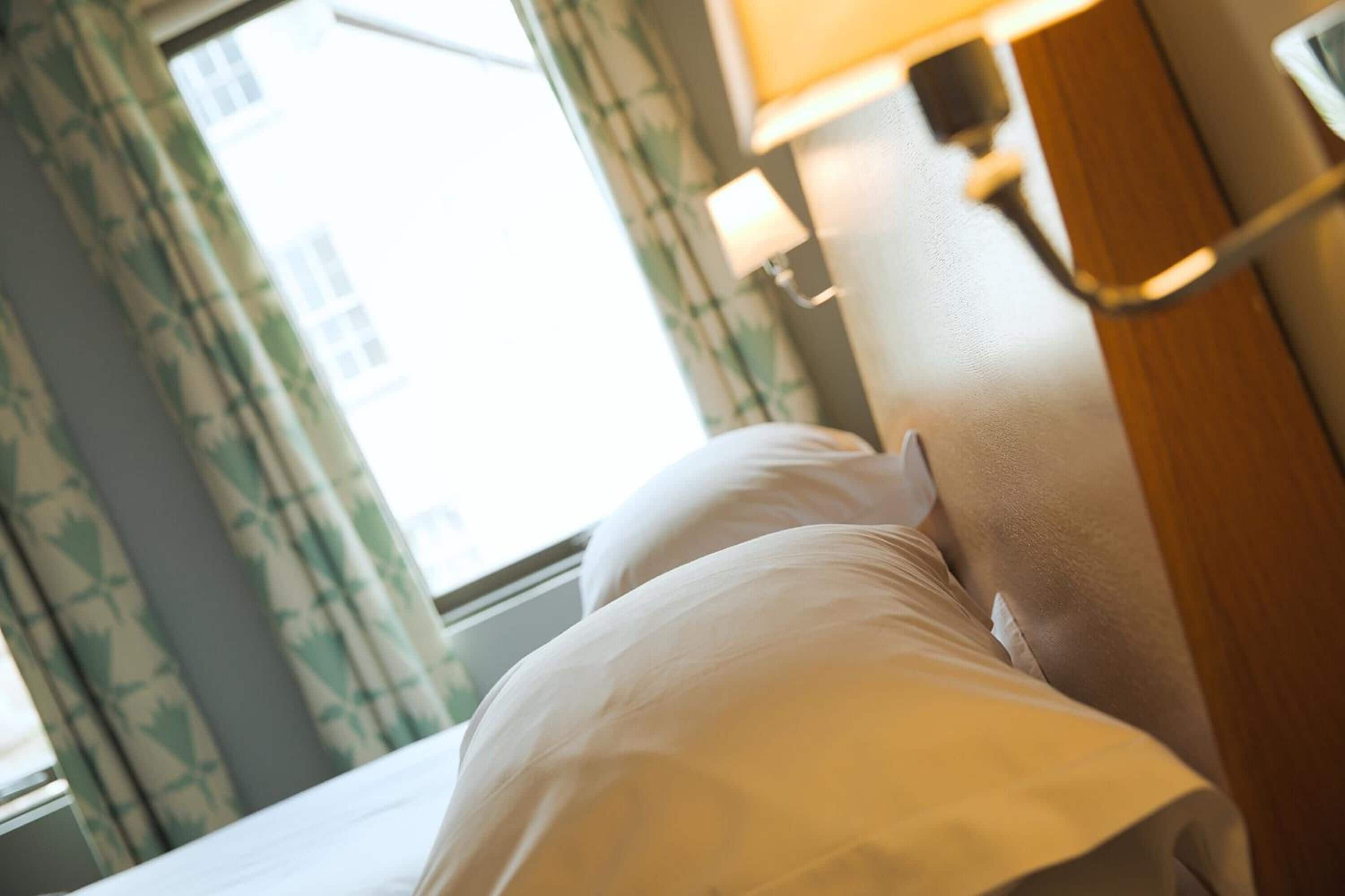 A hotel room with a bed, curtains, a window, and a lamp.