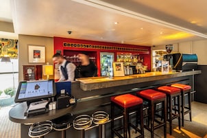 A bar area with a digital menu display, a coffee machine, and red bar stools.