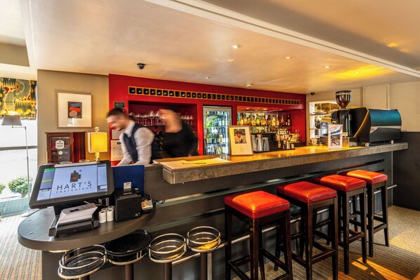 A bar area with a digital menu display, a coffee machine, and red bar stools.