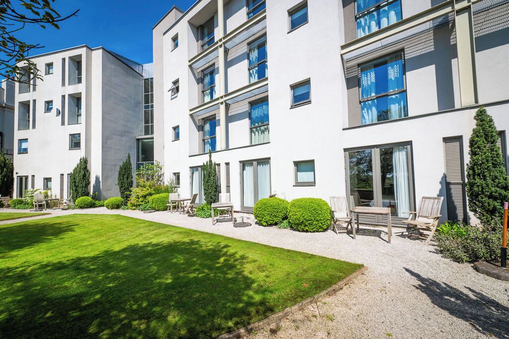 A modern multi-story residential building with a well-maintained lawn and outdoor seating area.