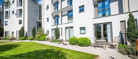 A modern multi-story residential building with a well-maintained lawn and outdoor seating area.