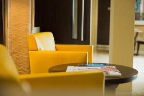 A yellow armchair and a round table with a magazine in a modern lobby with a textured wall and a dark door in the background. - Hart's Hotel (Nottingham)
