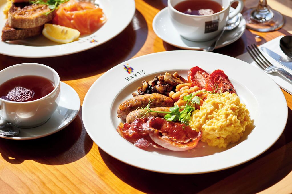 A breakfast setting with plates of food, a cup of tea, and a glass of water on a wooden table.