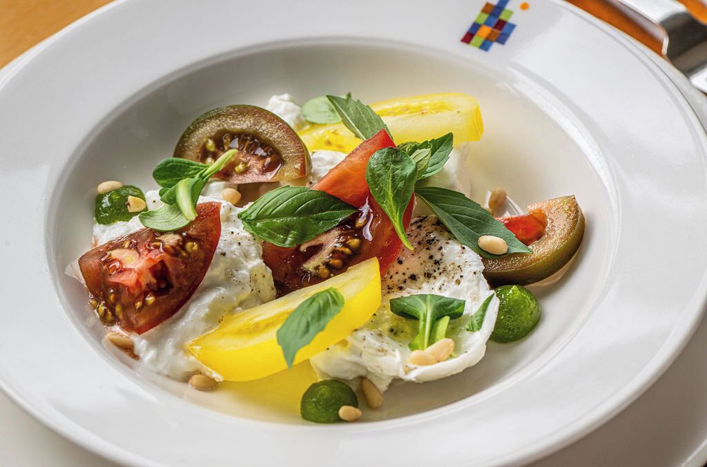 A white plate with a salad consisting of tomatoes, green leaves, and pine nuts.