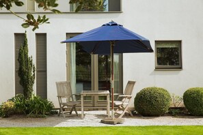An outdoor seating area with a table and chairs, a blue umbrella, and a white building with shutters and windows. - Hart's Hotel (Nottingham)
