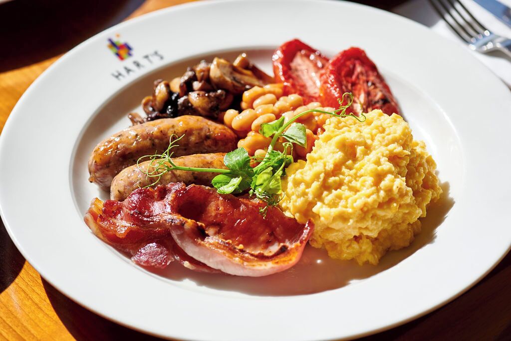 A plate of breakfast food including sausages, beans, bacon, and scrambled eggs.