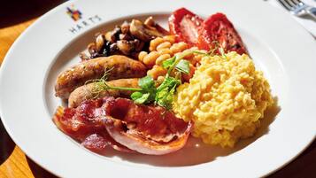 A plate of breakfast food including sausages, beans, bacon, and scrambled eggs.