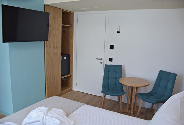 A hotel room with a bed, a TV mounted on a wooden wardrobe, a small table with two chairs, and a white door.