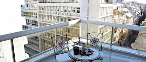 A balcony with a table and chairs, overlooking a cityscape with buildings.