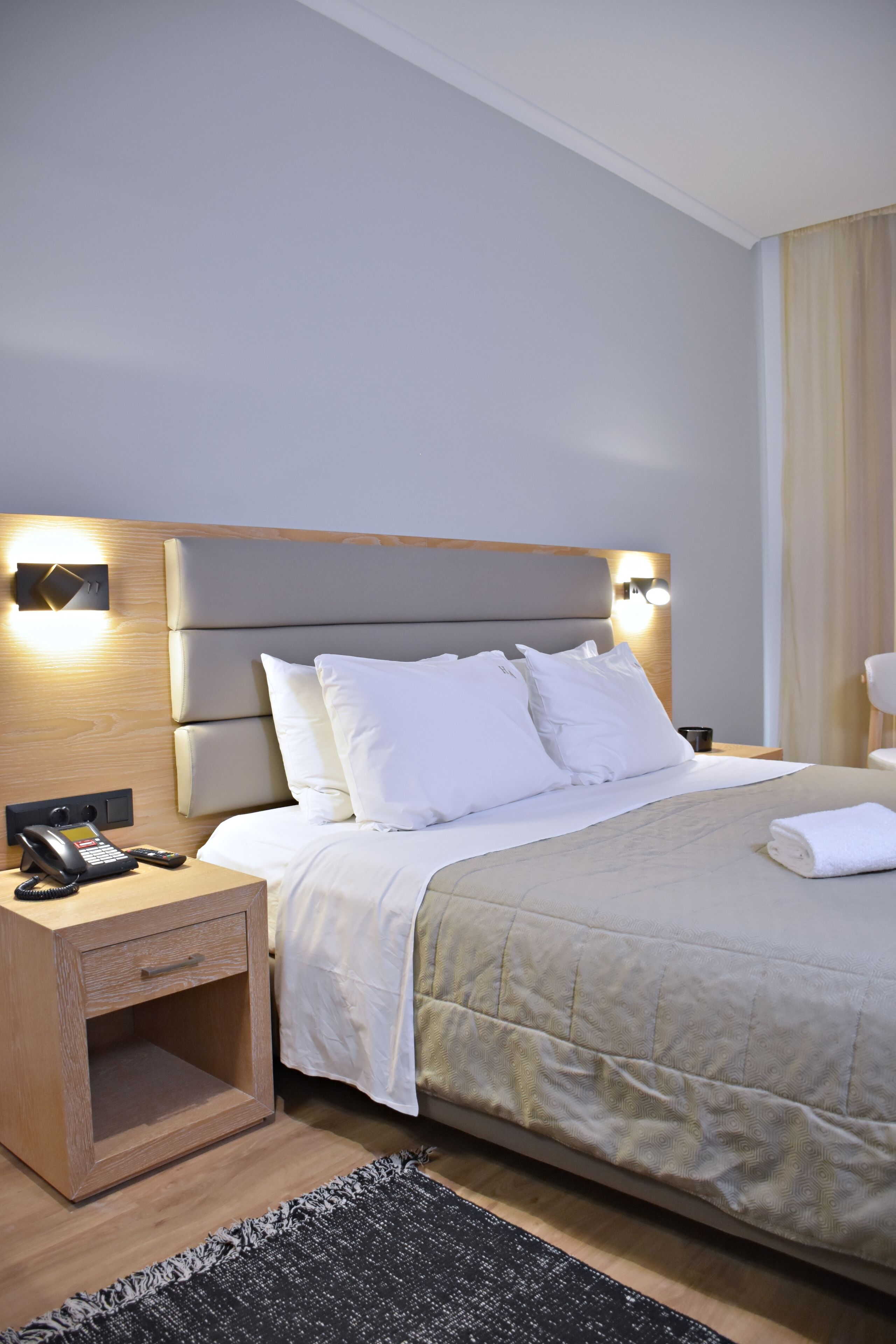 Una habitación de hotel con cama, mesita de noche, lámpara y teléfono.