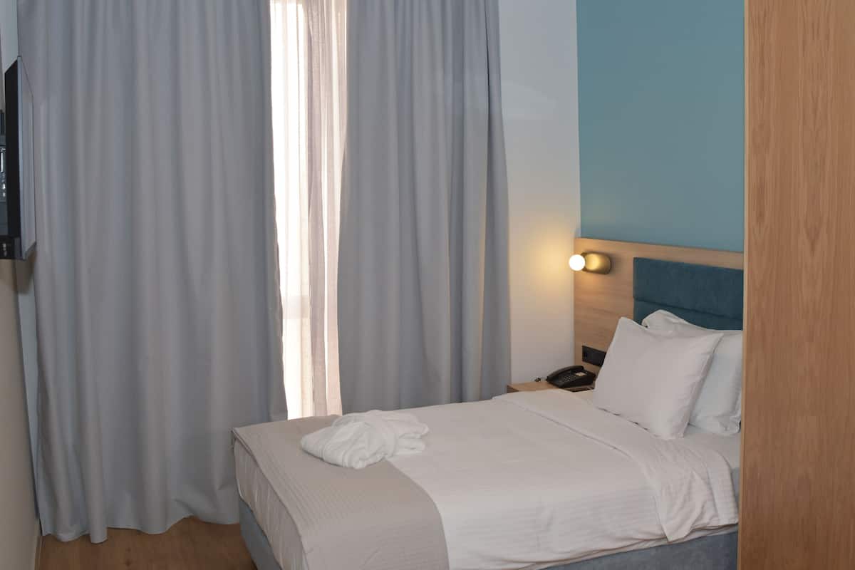 Une chambre d’hôtel avec un lit, une table de chevet, un téléphone et des rideaux.