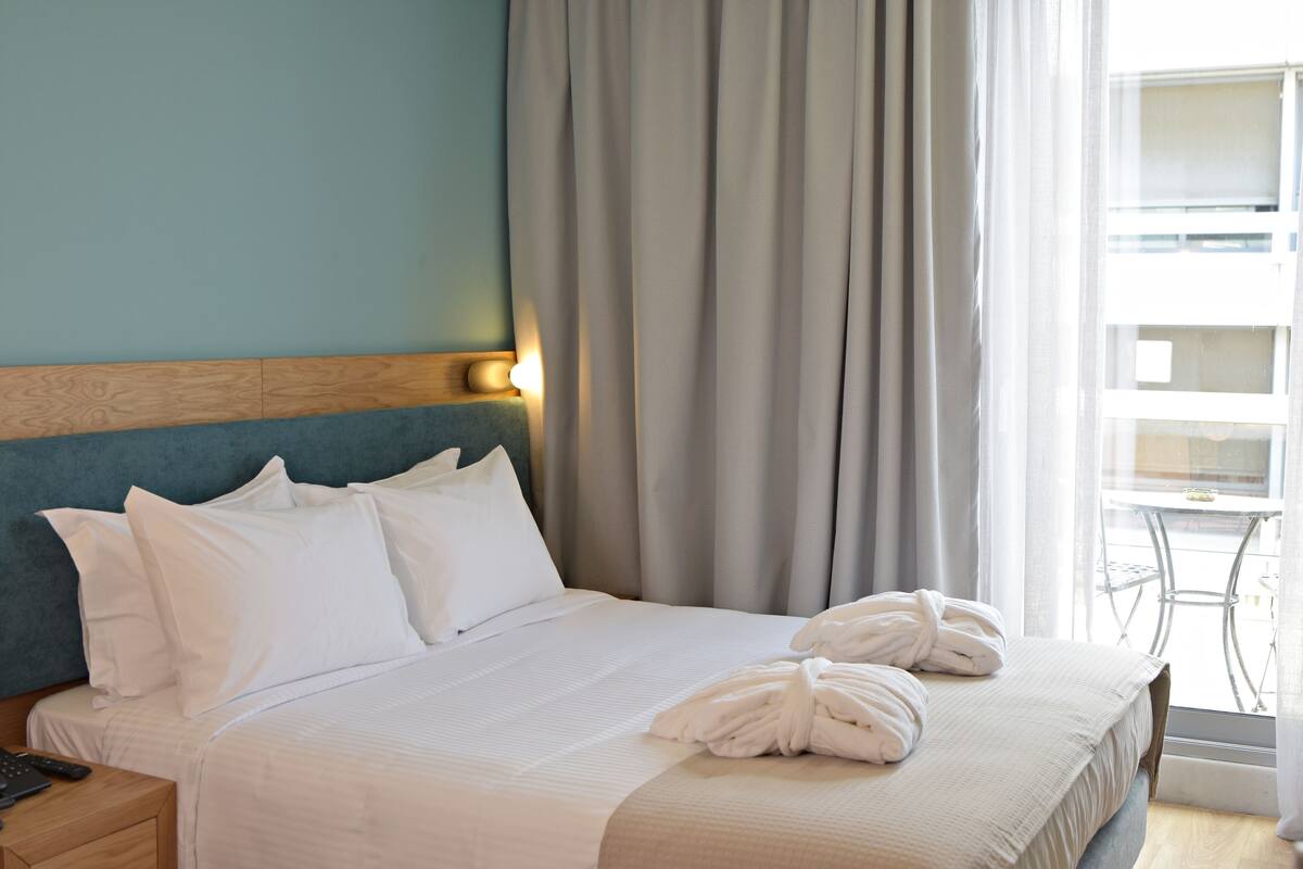 Un lit bien fait, avec du linge de lit et des serviettes blanches, une tête de lit en bois et une table de chevet avec une lampe.