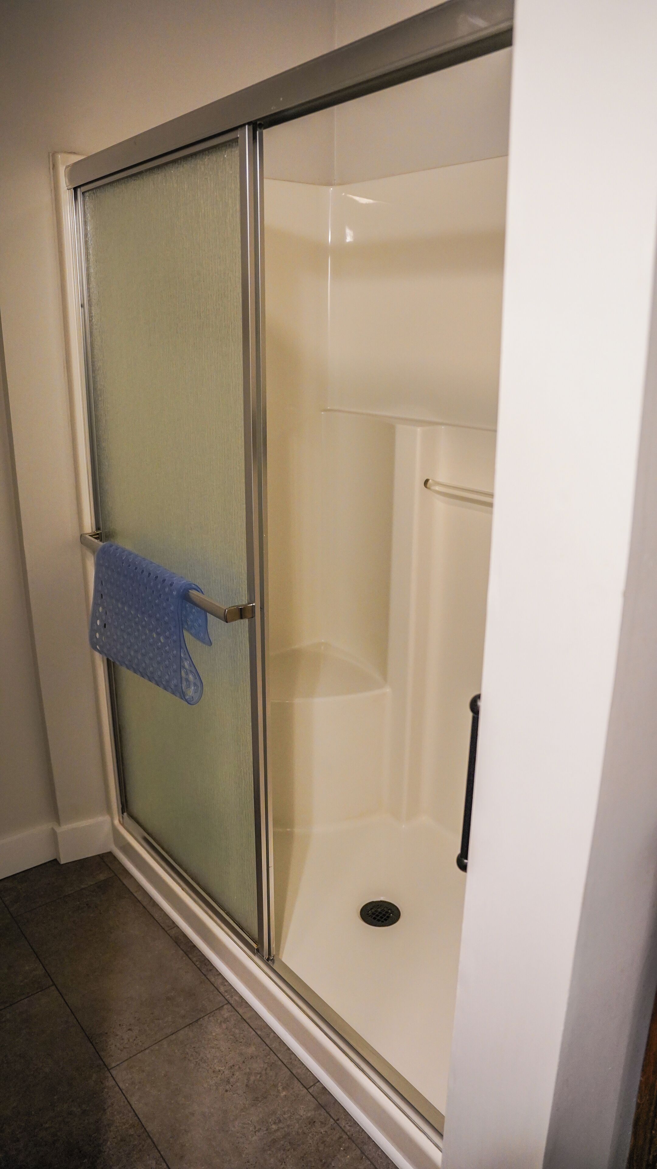 A glass-enclosed shower with a towel rack and a drain.