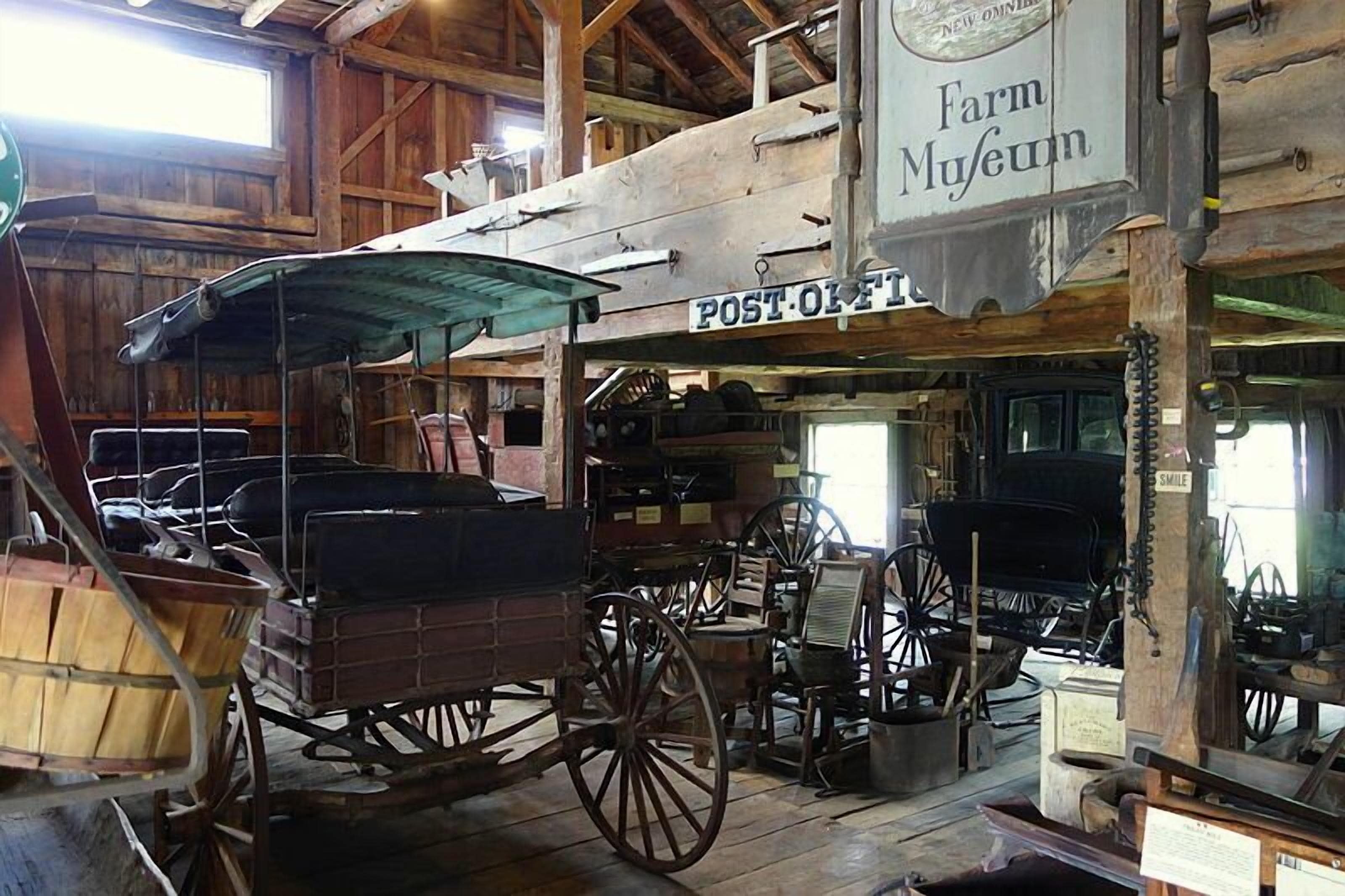 A rustic barn interior with wooden beams, a post office sign, and vintage farm equipment.