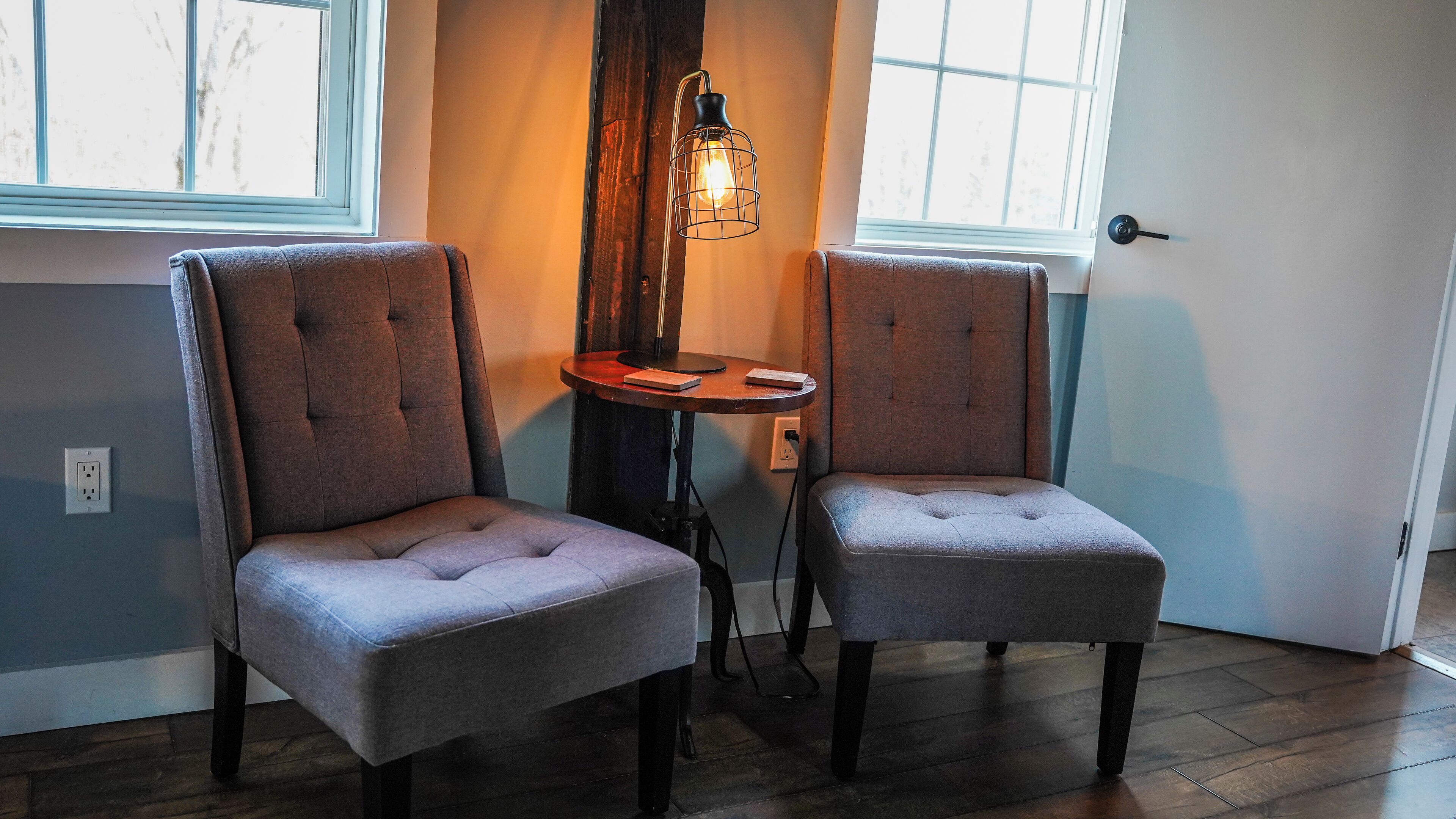 Two upholstered chairs with a cushioned seat and backrest, positioned next to a wooden table with a light fixture above.