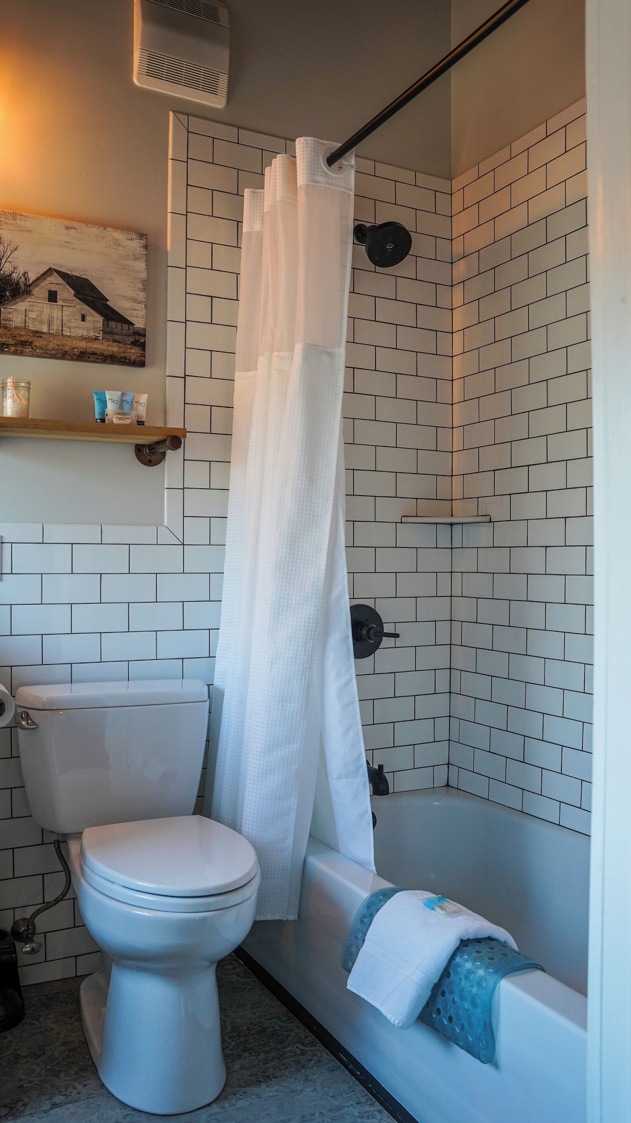 Baño con inodoro, ducha y bañera, con azulejos blancos y cortina de ducha colgante.