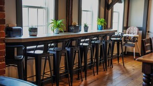 A bar area with wooden stools, a long counter, and potted plants. - Old Mill Inn (Hatfield)