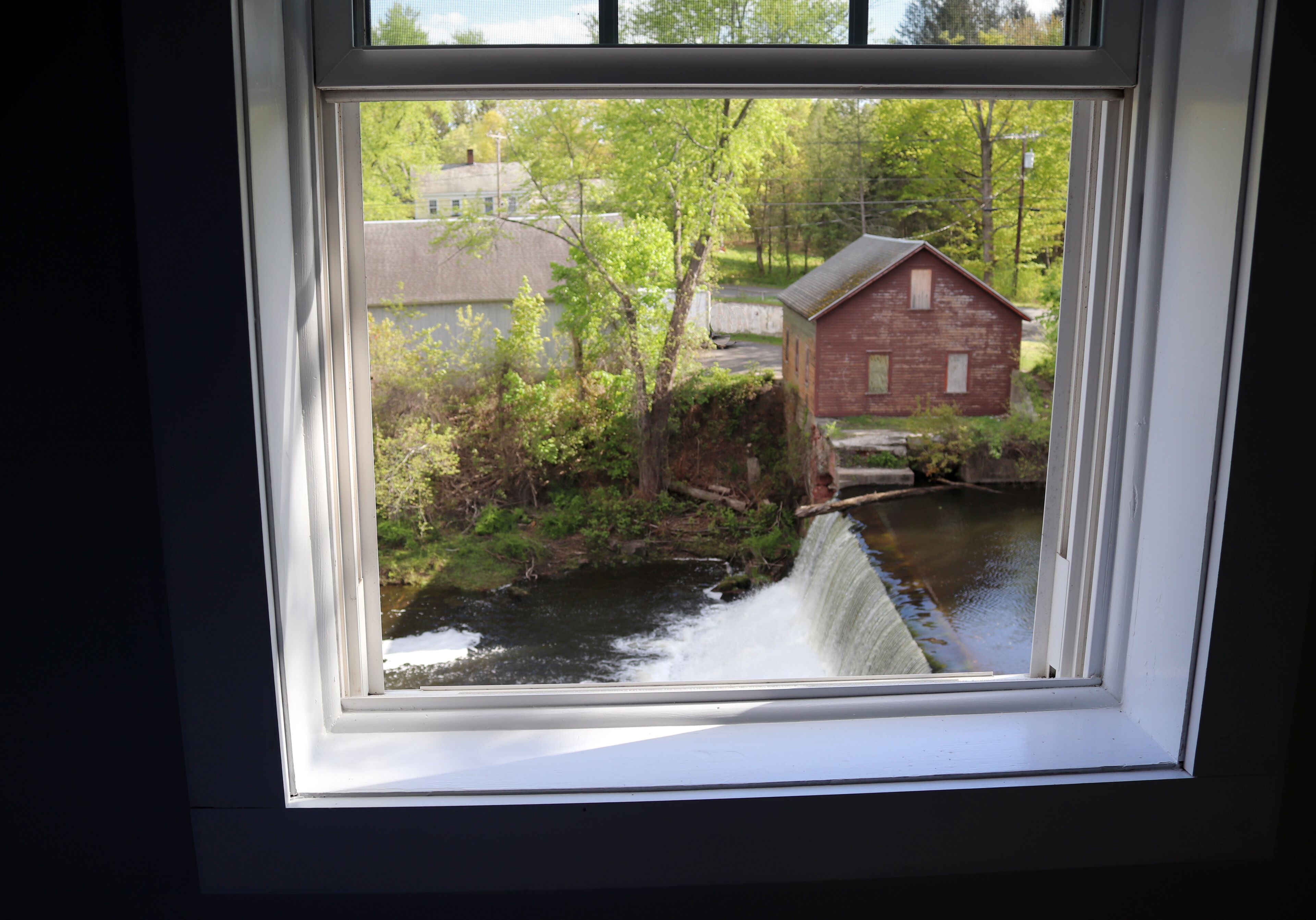 Blick durch ein Fenster auf einen Fluss, eine Holzkonstruktion und viel Grün.