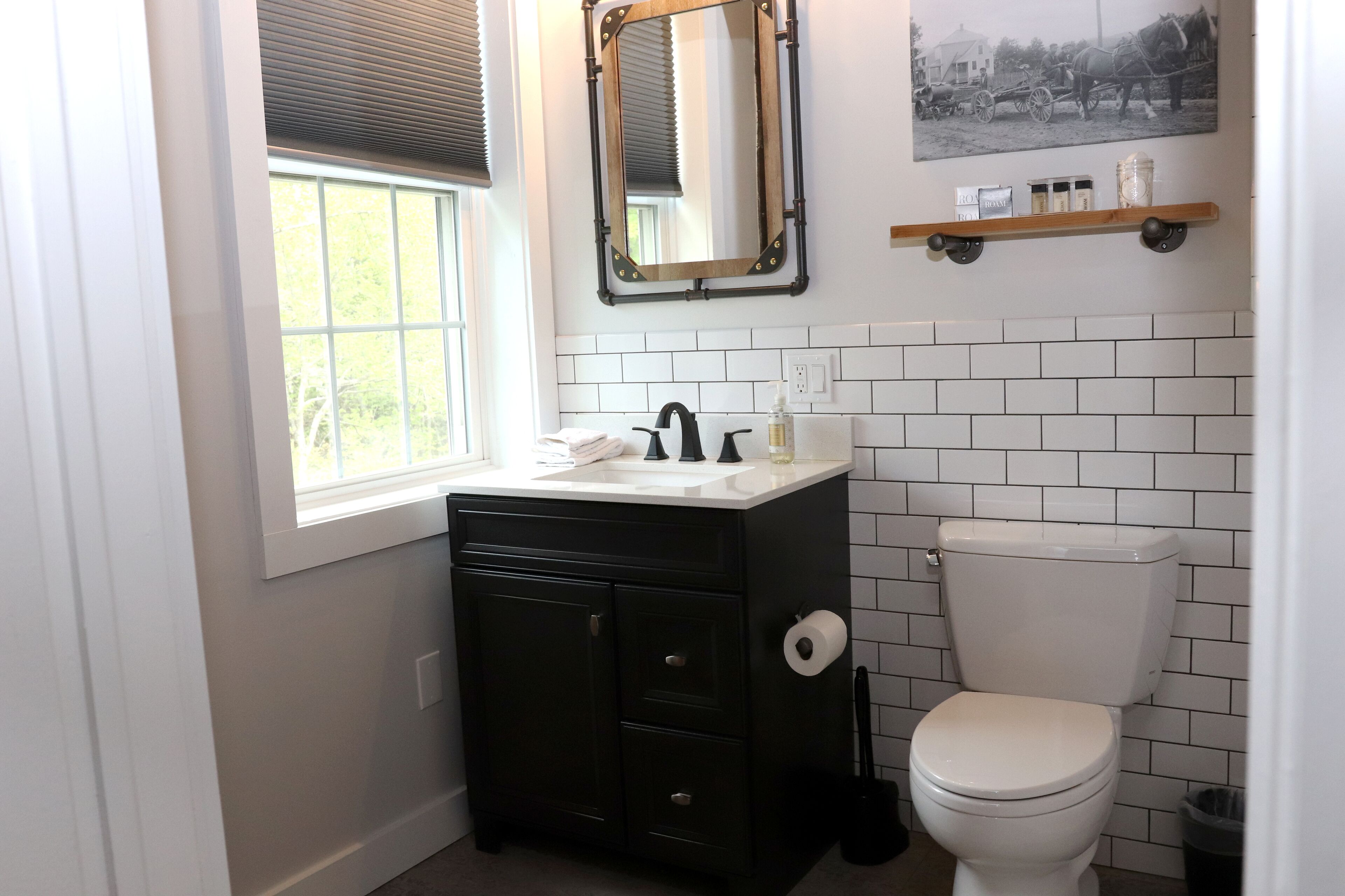 Une salle de bain avec un meuble-lavabo noir, des toilettes blanches et une fenêtre avec des stores.