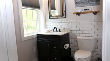 Une salle de bain avec un meuble-lavabo noir, des toilettes blanches et une fenêtre avec des stores.