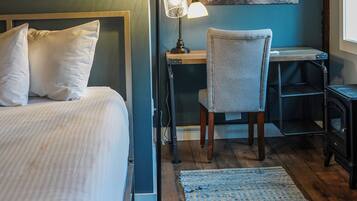 A bedroom with a bed, bedside table, lamp, chair, and a painting on the wall.