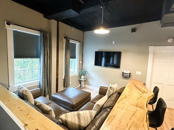 A modern living room with a sofa set, a wooden coffee table, a television mounted on the wall, and a door.