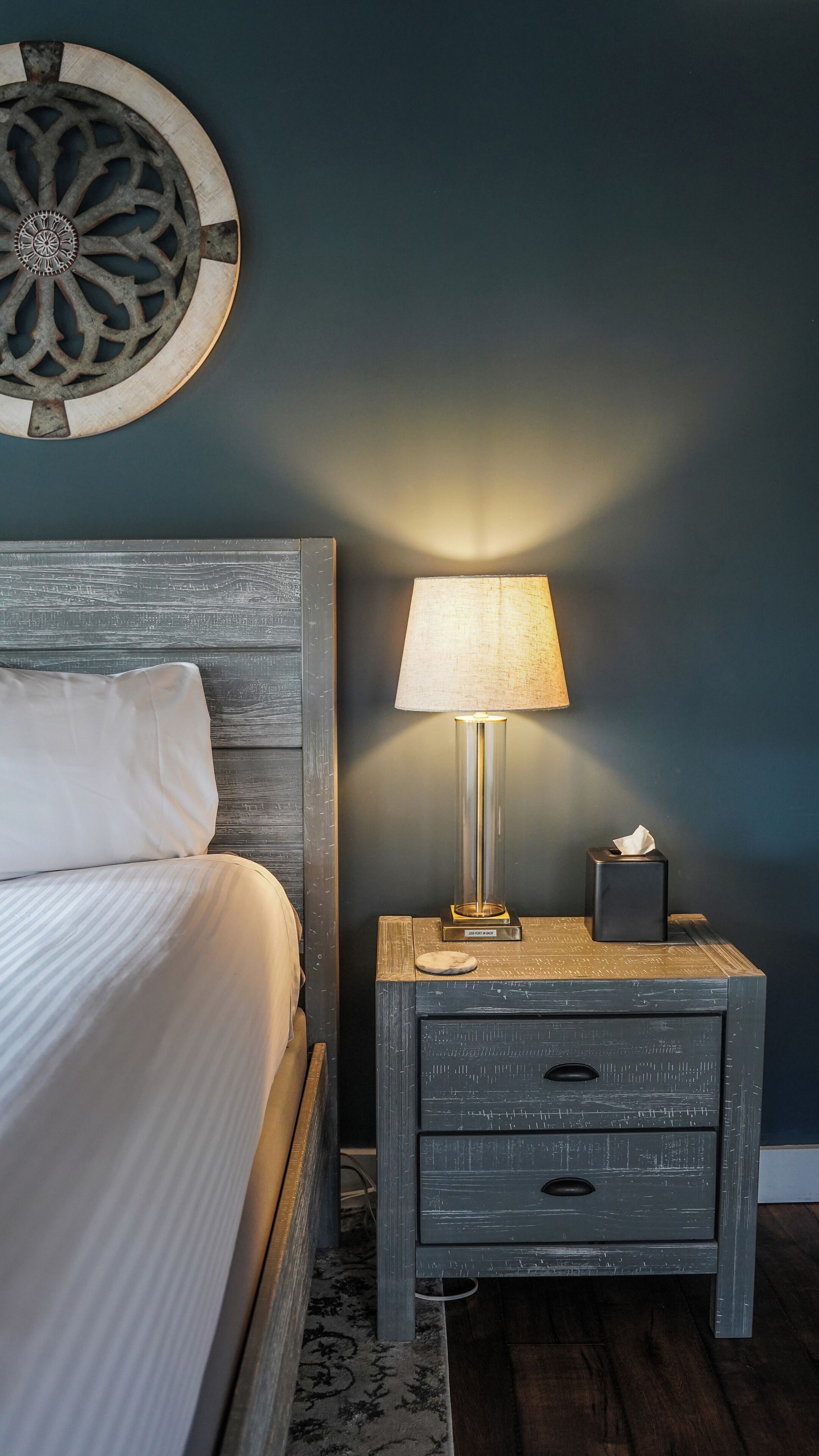 A bedroom with a bed, a nightstand, a lamp, and a decorative wall piece.