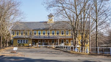 A yellow building with a clock tower, a porch, and a fenced area.