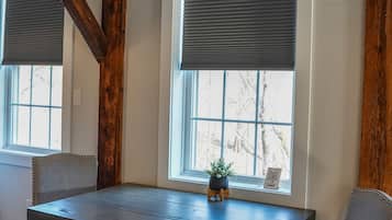 Un comedor con mesa y sillas de madera, ventanas amplias con persianas y vigas de madera a la vista en el techo.