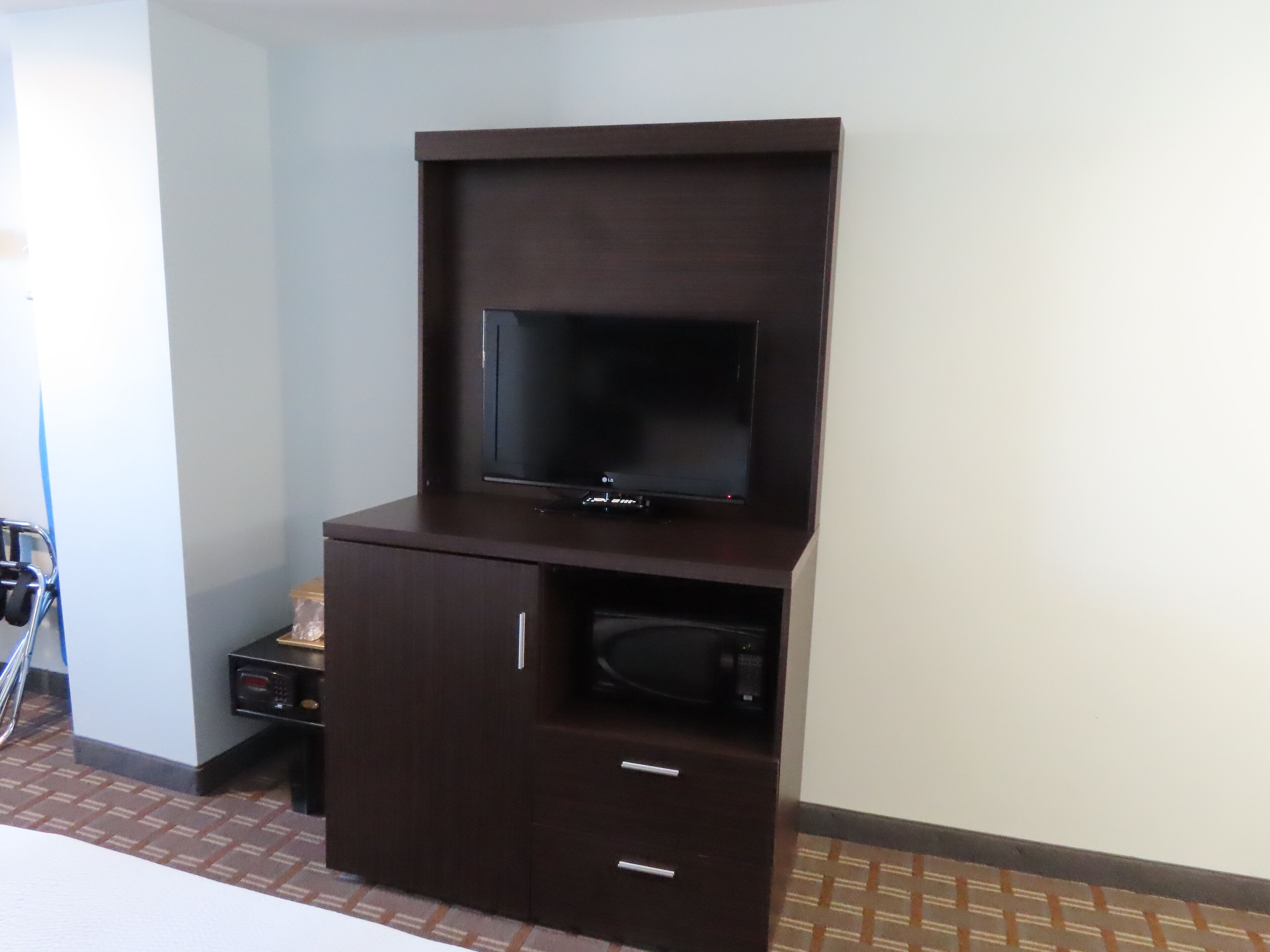 A dark wooden entertainment unit with a flat-screen TV, a microwave, and a small drawer.