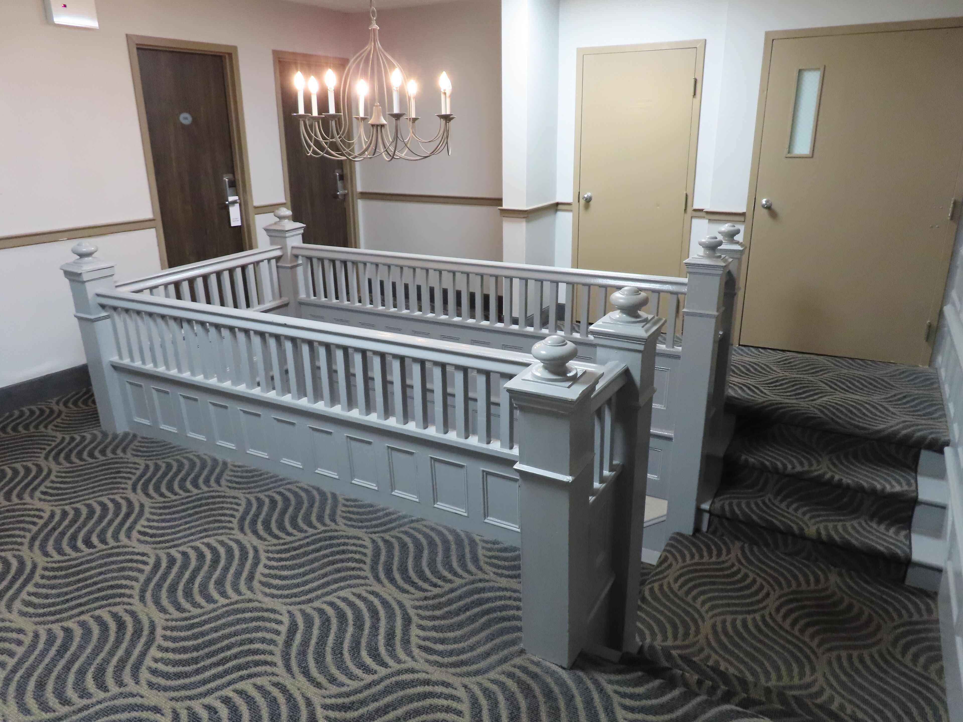 Ein Hotelzimmer mit einem weißen Bett, einer Kristallleuchter, einem gemusterten Teppich und einer Tür mit einer satinierten Glasscheibe.