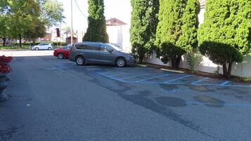 A parking lot with several cars, including a gray minivan and a red SUV. There are tall, narrow trees lining the parking area.
