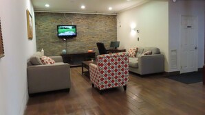 A living room with a stone wall, a television, two sofas, a patterned armchair, and a wooden floor. - St. Charles Hotel (Hudson)