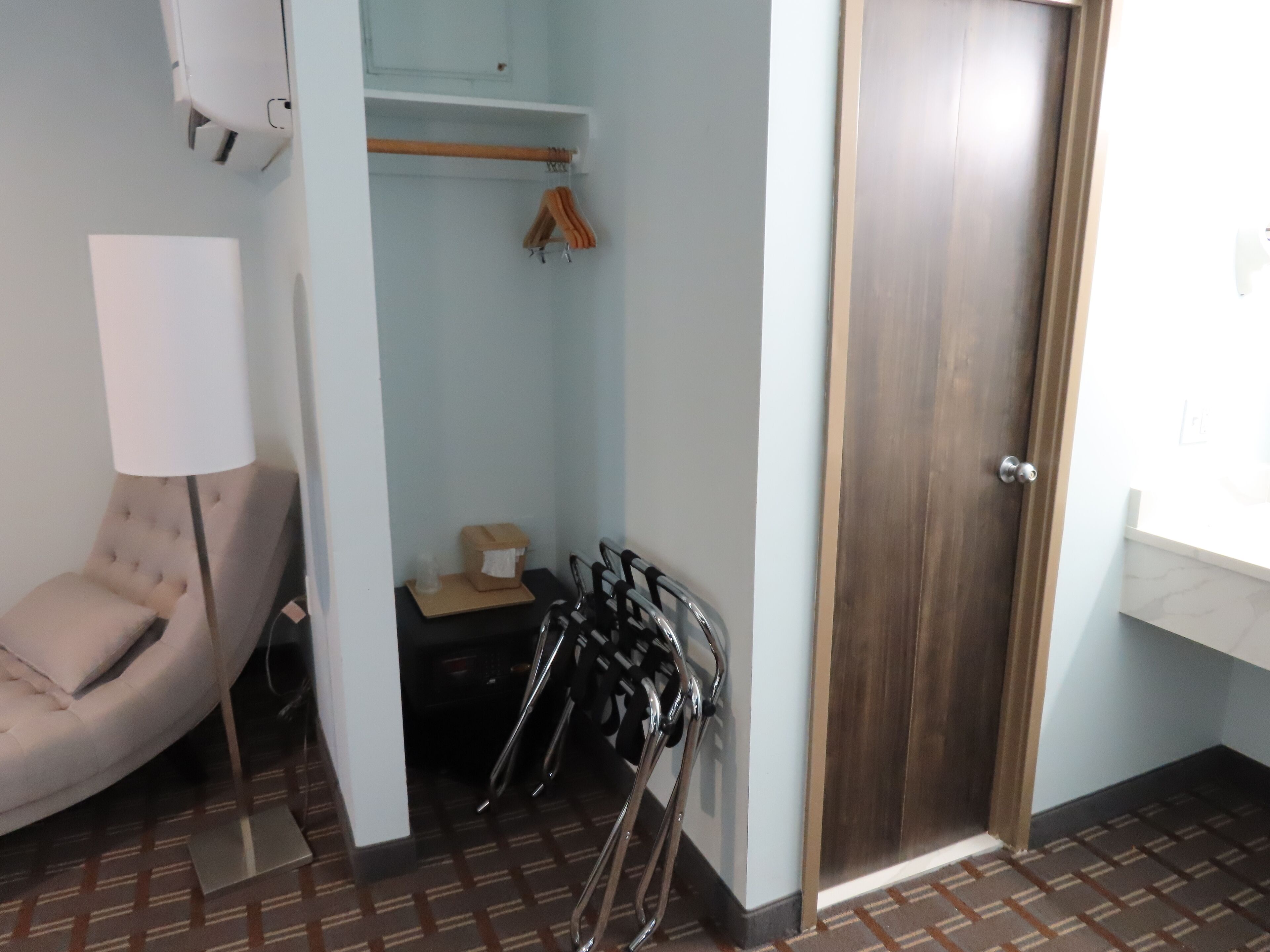 Ein kleines Zimmer mit Stuhl, Tisch, Kleiderhaken und einer Tür.