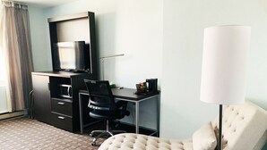 A hotel room with a desk, chair, TV, lamp, and a patterned carpet. - St. Charles Hotel (Hudson)