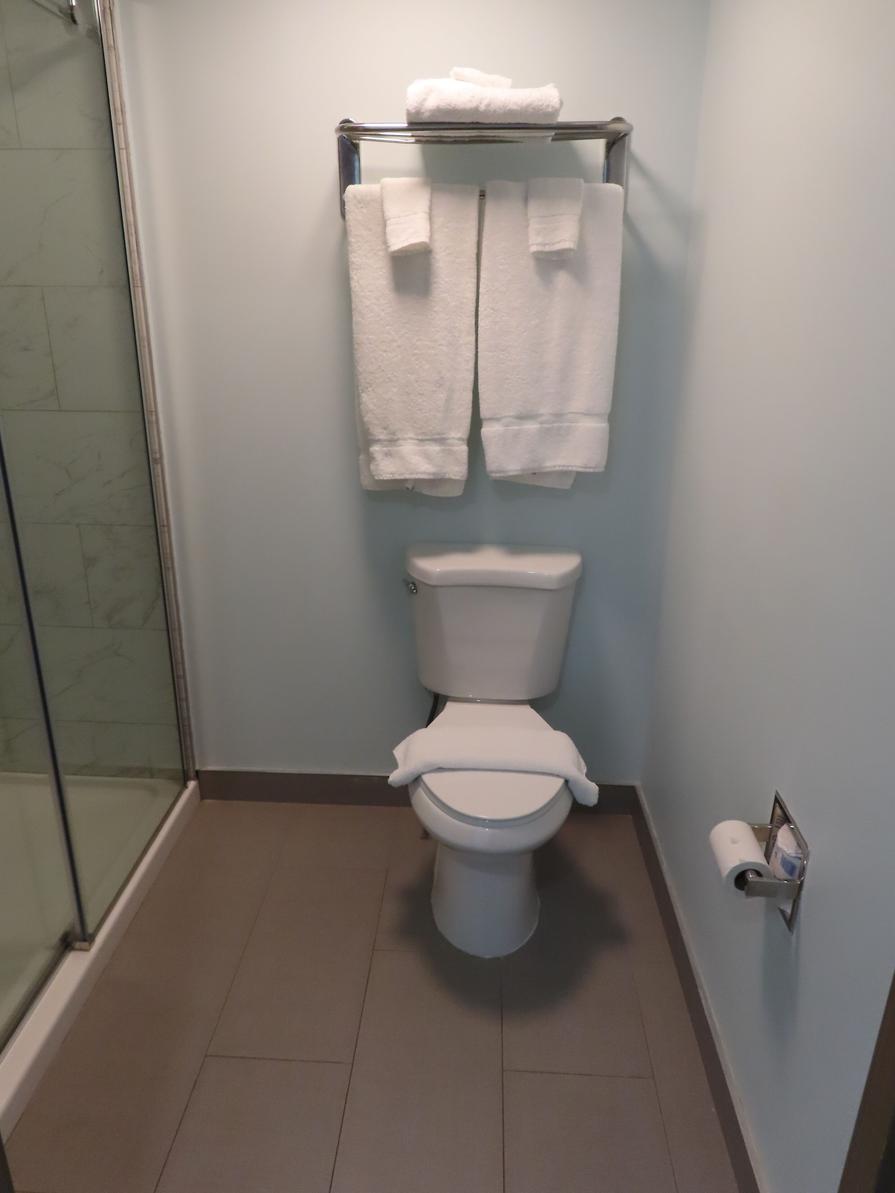 A bathroom with a toilet, a towel rack with towels, and a toilet paper holder.