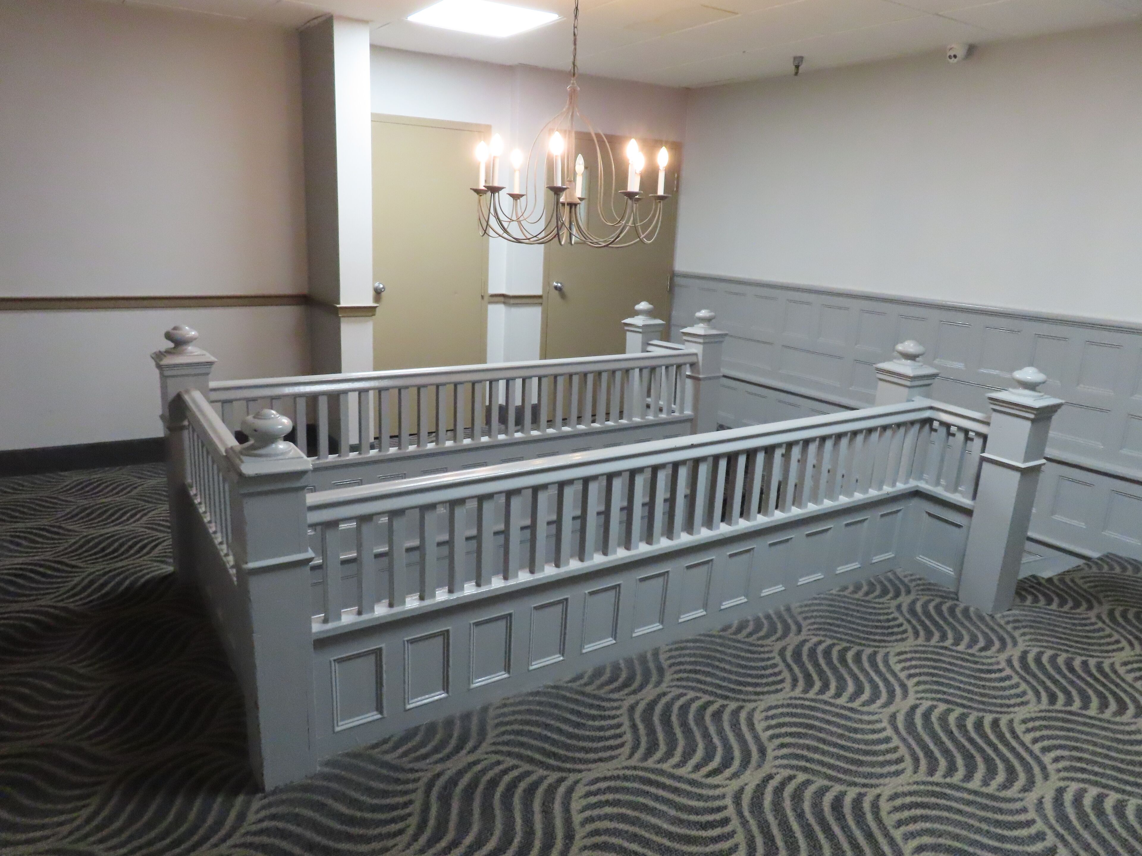 A room with a white bed, a chandelier, and a patterned carpet.