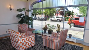 A room with striped armchairs, a patterned sofa, and a glass table. There are potted plants on the windowsill and a view of the street outside. - St. Charles Hotel (Hudson)