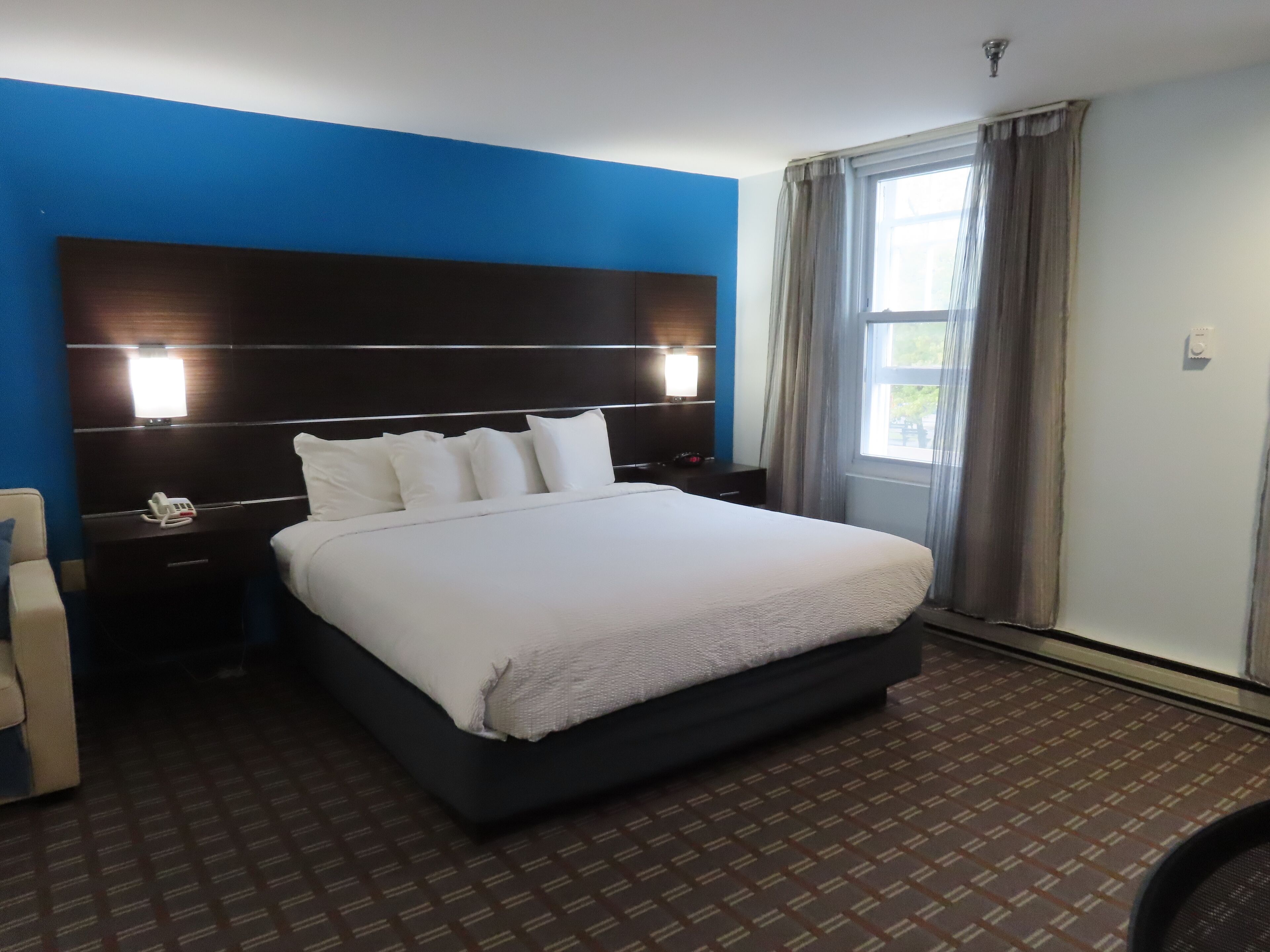 A hotel room with a large bed, a bedside table with a lamp, and a window with curtains.