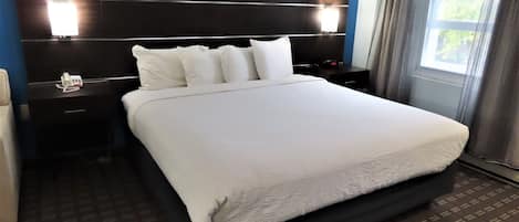 Una habitación de hotel con una cama grande, un cabecero oscuro, lámparas de noche, una mesita de noche y una ventana con cortinas.