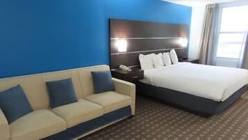 A hotel room with a bed, a sofa, a nightstand, and a wall-mounted lamp.