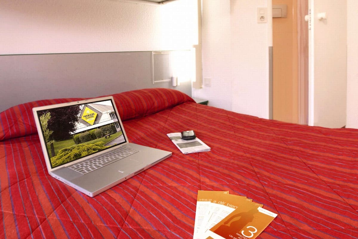 Une chambre d’hôtel équipée d’un lit, d’un ordinateur portable, d’un téléphone intelligent et d’un ensemble de brochures.