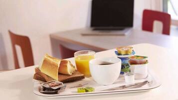 Ein Frühstücksbrett mit Toast, Saft, Kaffee und Joghurt auf einem weißen Tisch.