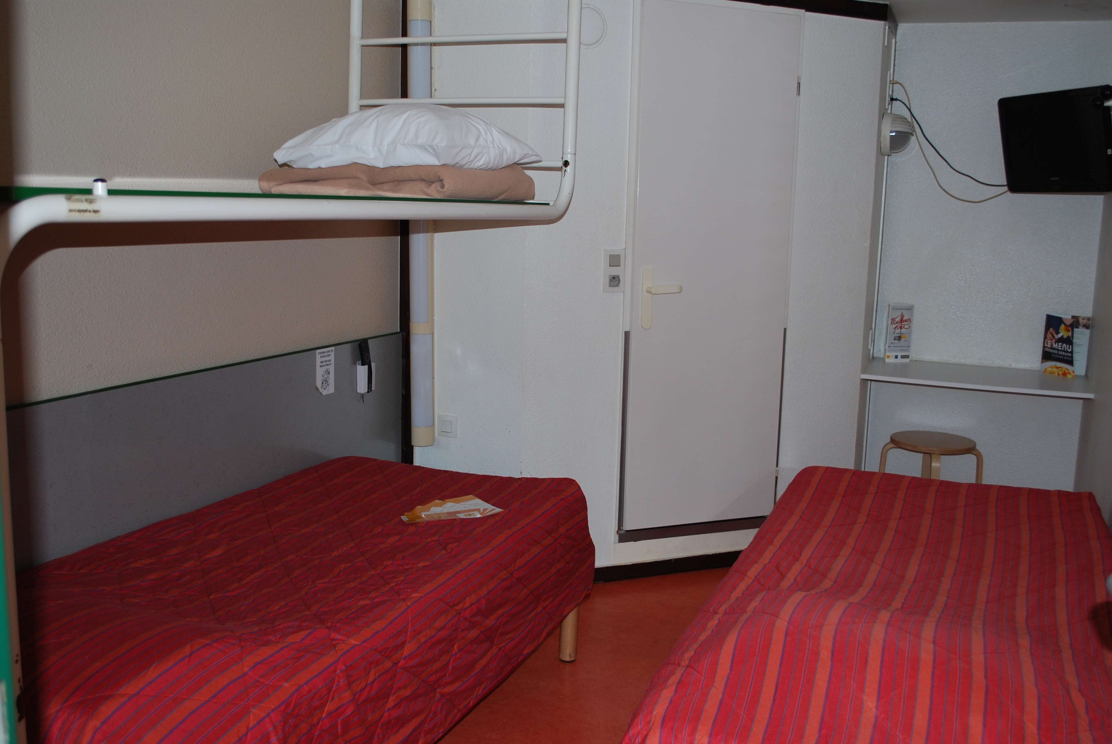 A dormitory room with bunk beds, a desk, and a television.