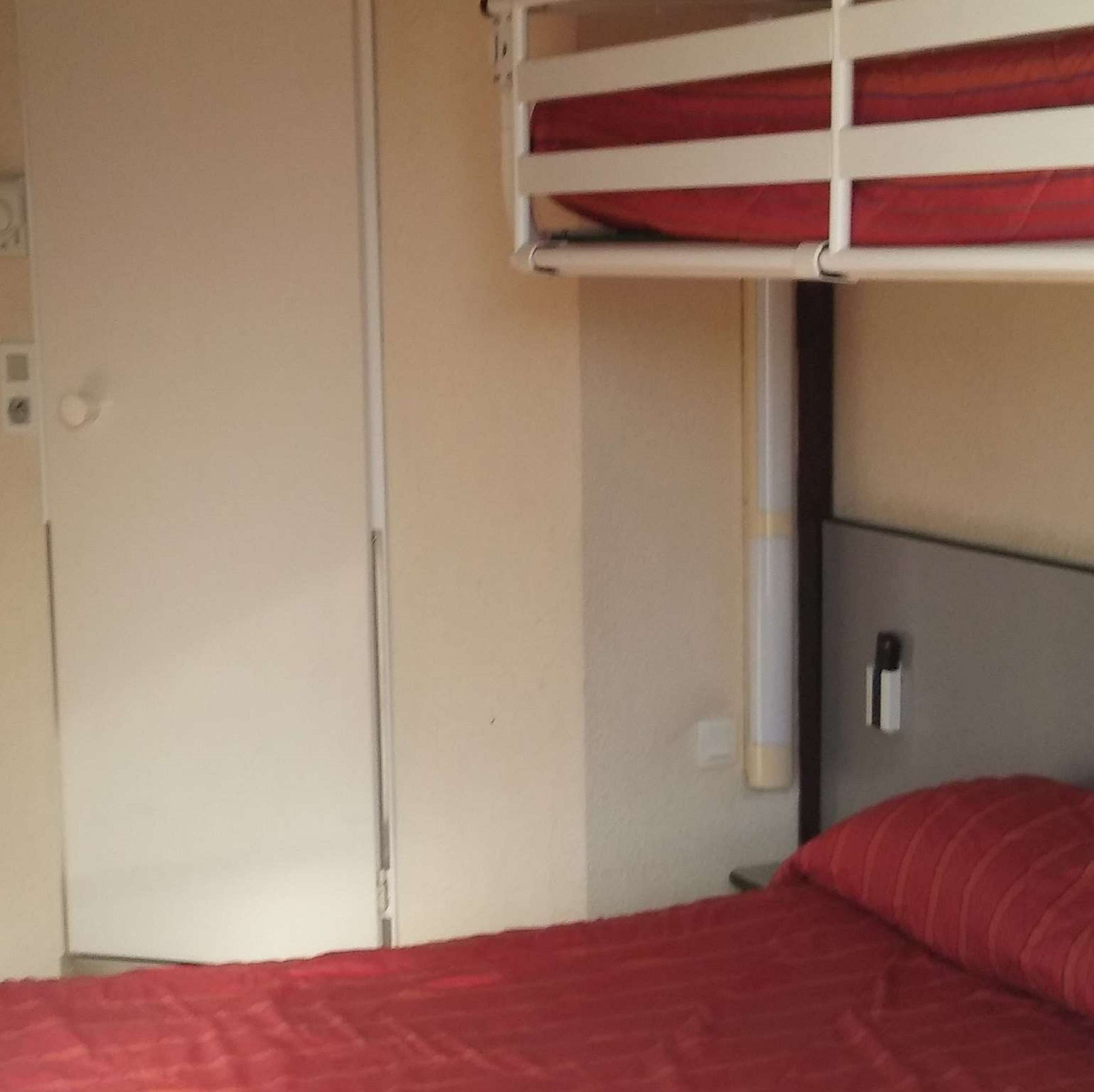 A bunk bed with a red mattress and a white headboard.